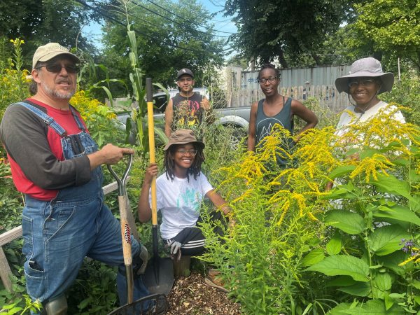 Five people pose with shovels in a garden