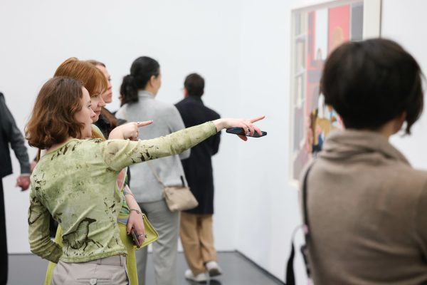 Several people in a gallery space. One person points to a painting on a white wall.