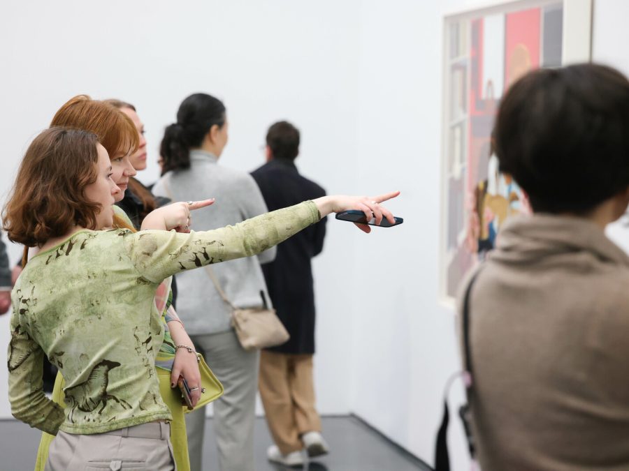 Several people in a gallery space. One person points to a painting on a white wall.