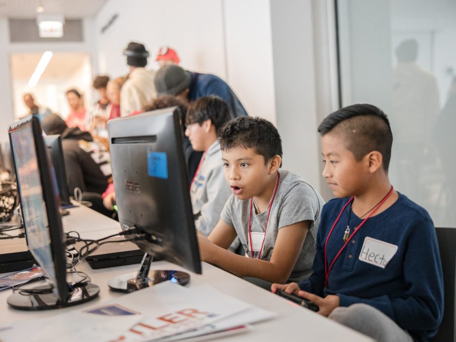 Two kids sit immersed in a computer screen, one with mouth agape