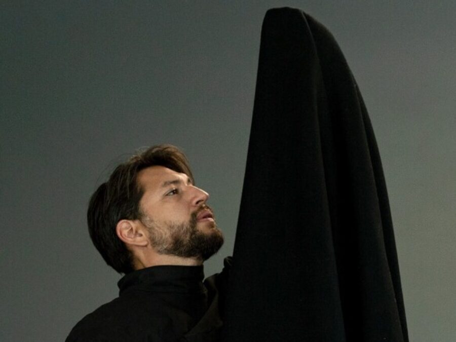 A man dressed in black holds a large black fabric up above his head
