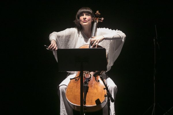 A woman playing a cello is dramatically lit against a black background.