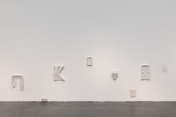 Installation of several white abstract artworks on a white gallery wall