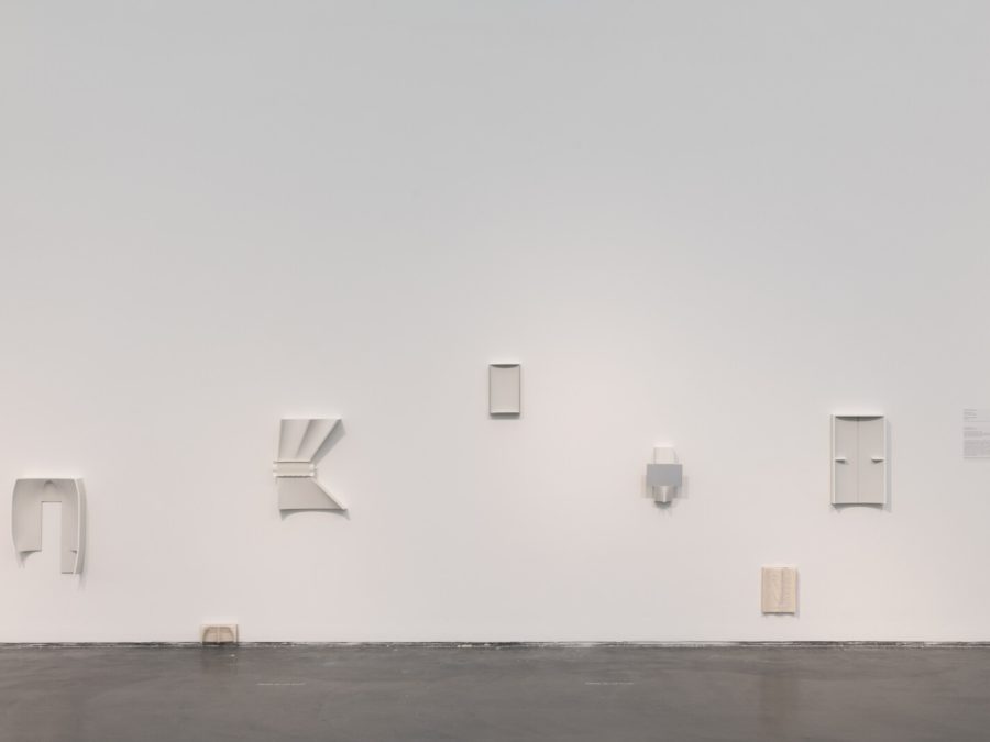 Installation of several white abstract artworks on a white gallery wall