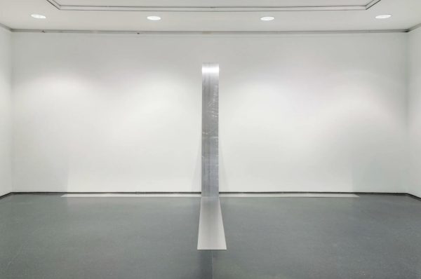 A flat, silver sculptural artwork that extends from the floor up the wall, almost to the ceiling.