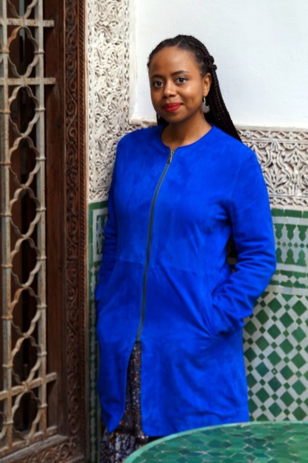 Photograph of a Black female-presenting person in a long vibrant blue jacket.
