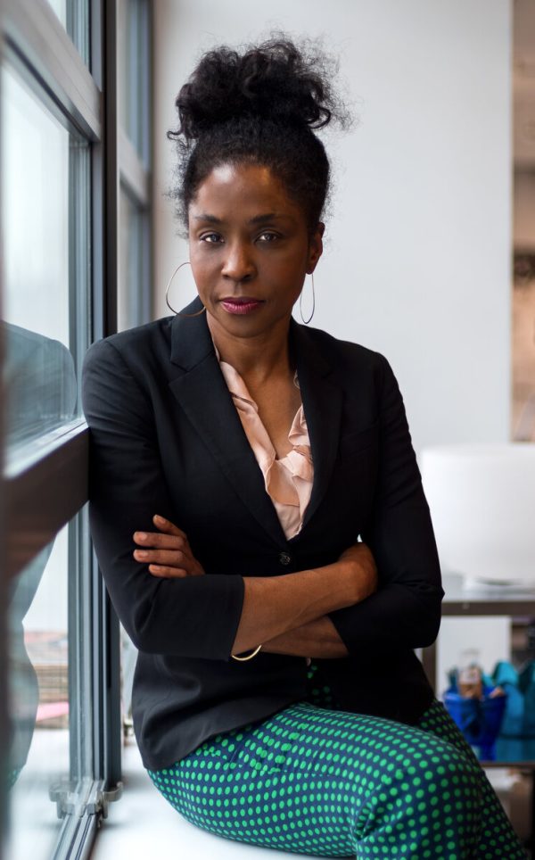 A Black woman sitting next to a window with her arms crossed