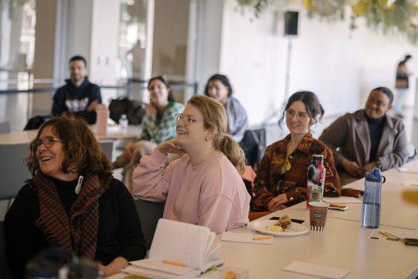 People sitting in a row at a table smiling at something off camera