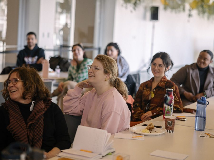 People sitting in a row at a table smiling at something off camera