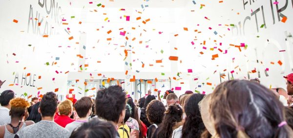 Confetti falls over a crowd of people in a bright white room