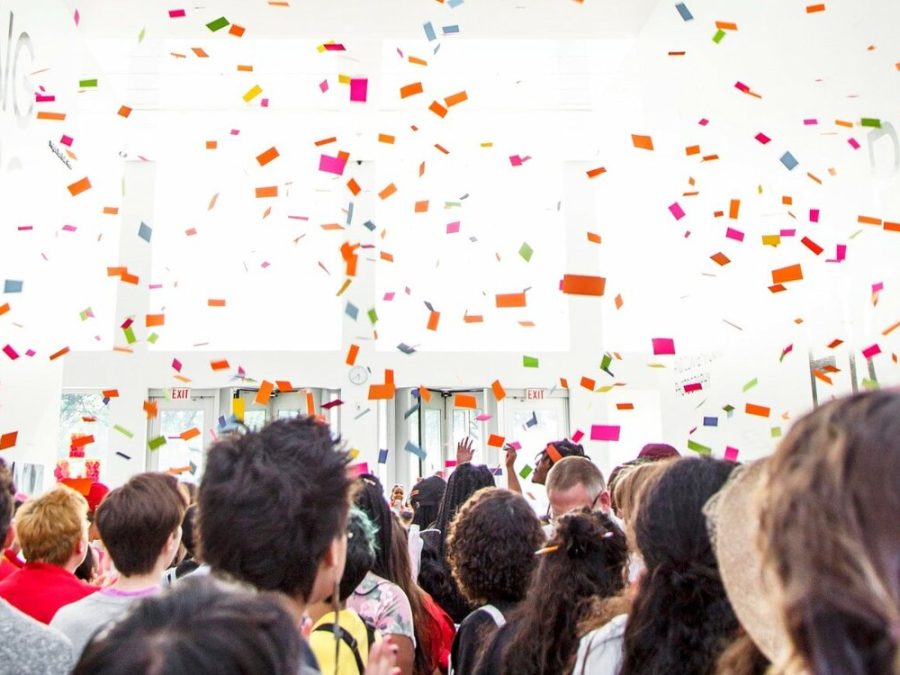 Confetti falls over a crowd of people in a bright white room