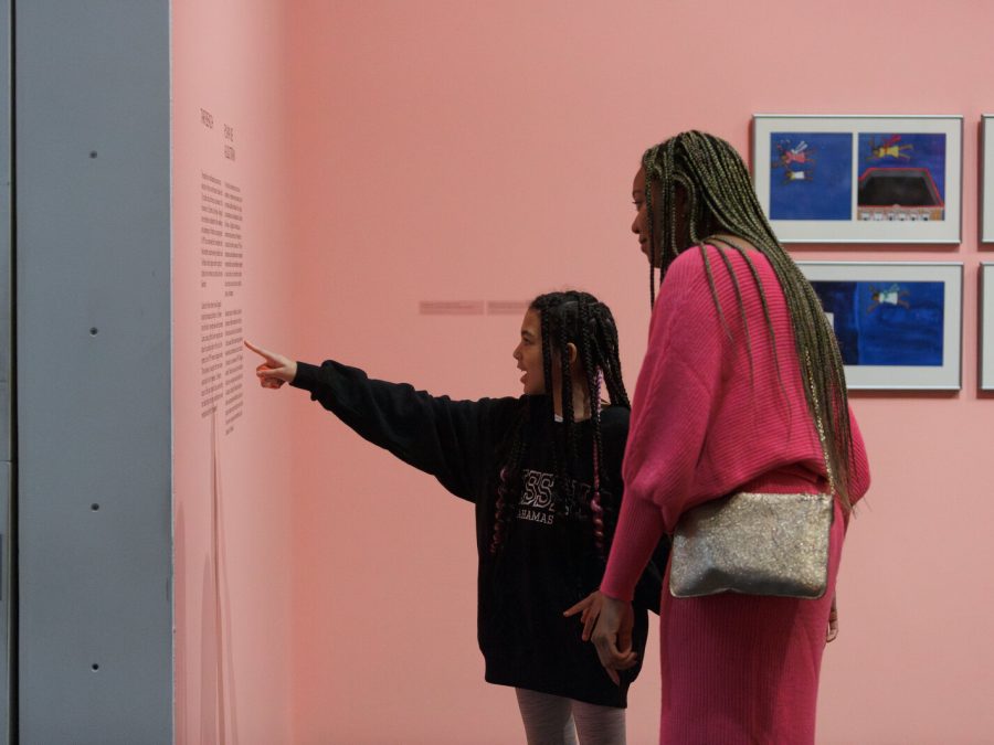 A younger person points to text on a pink wall and the guardian they are with leans in to read.
