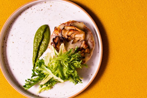 A small salad and a mushroom torte on a white plate against a light orange background