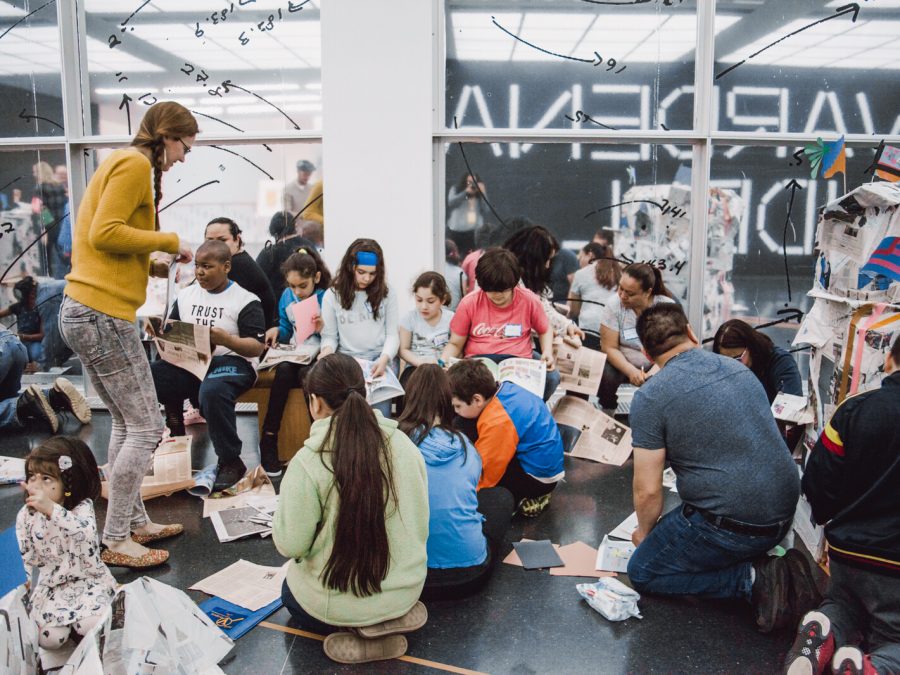 Kids and adults sit on the floor with artmaking supplies.