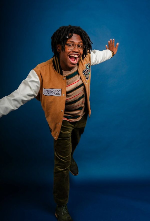 Portrait of a young Black man against a teal backdrop.