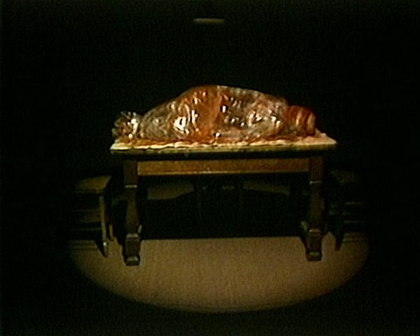 A colorful object rests on a table in a dark room lit by one spotlight