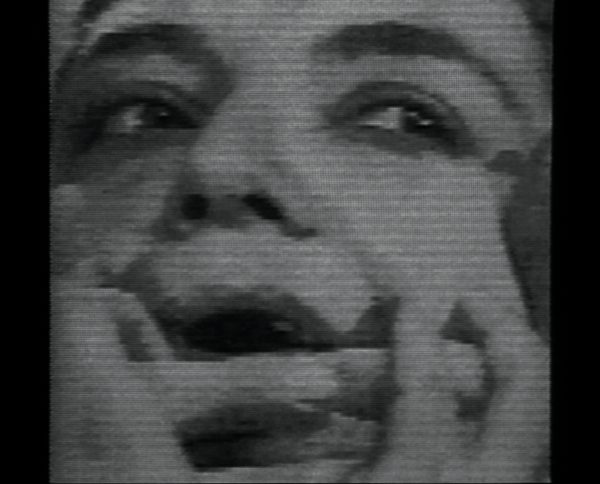Still of Black-and-white video of a close of up a person's face with their mouth open as two hands hold an object in it