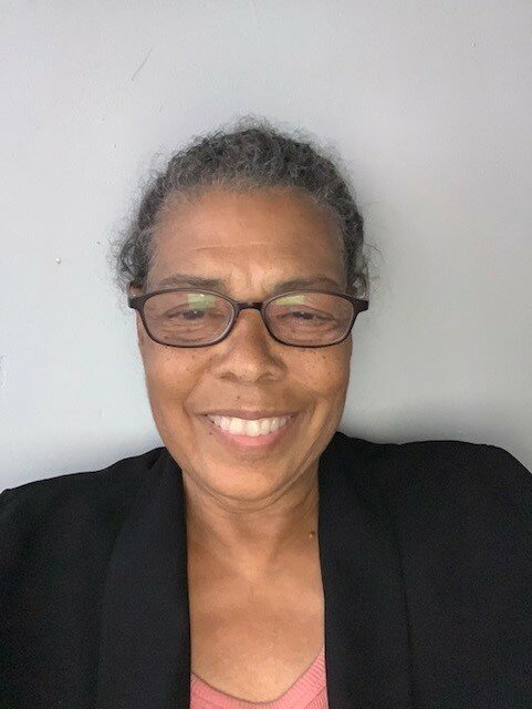 Portrait of a light-skinned Black woman with her hair pulled against a gray background.