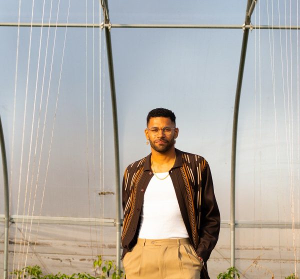 Portrait of a Black man standing within a steel hoop greenhouse system.