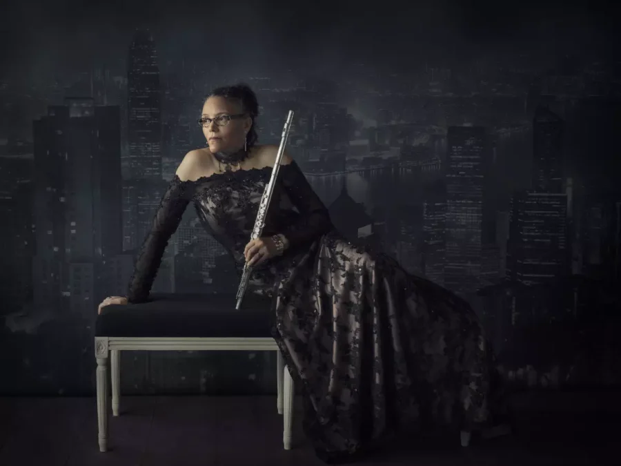 portrait of Nicole Mitchell in a black, long-sleeved gown sitting on a bench holding a flute against a dark background