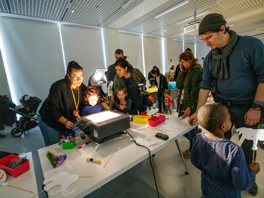 Kids and adults gather in a darkened room around a projector