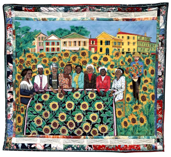 Quilt featuring a group of people with various tones of brown skin in a field of sunflowers in front of a small block of houses