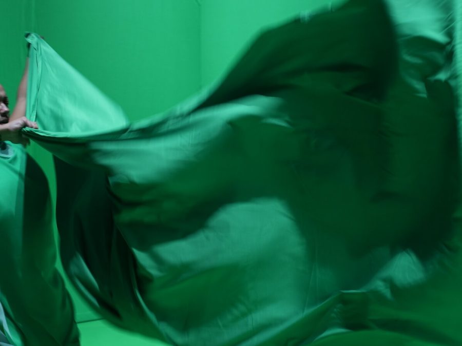 A person dressed in green in a green room holds a billowing green sheet in front of them