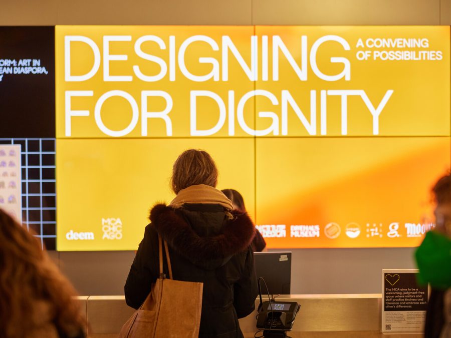 A person stands in front of a digital sign that reads DESIGNING FOR DIGNITY.
