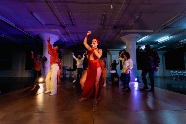 A group of people captured in motion with their right hands raised in the air in the middle of a dimly lit dance floor.