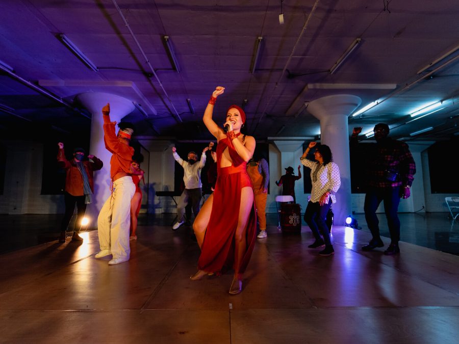 A group of people captured in motion with their right hands raised in the air in the middle of a dimly lit dance floor.