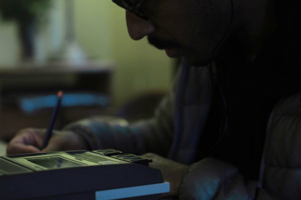 Close up of a man posed to write as he sits in front of a tape recorder.
