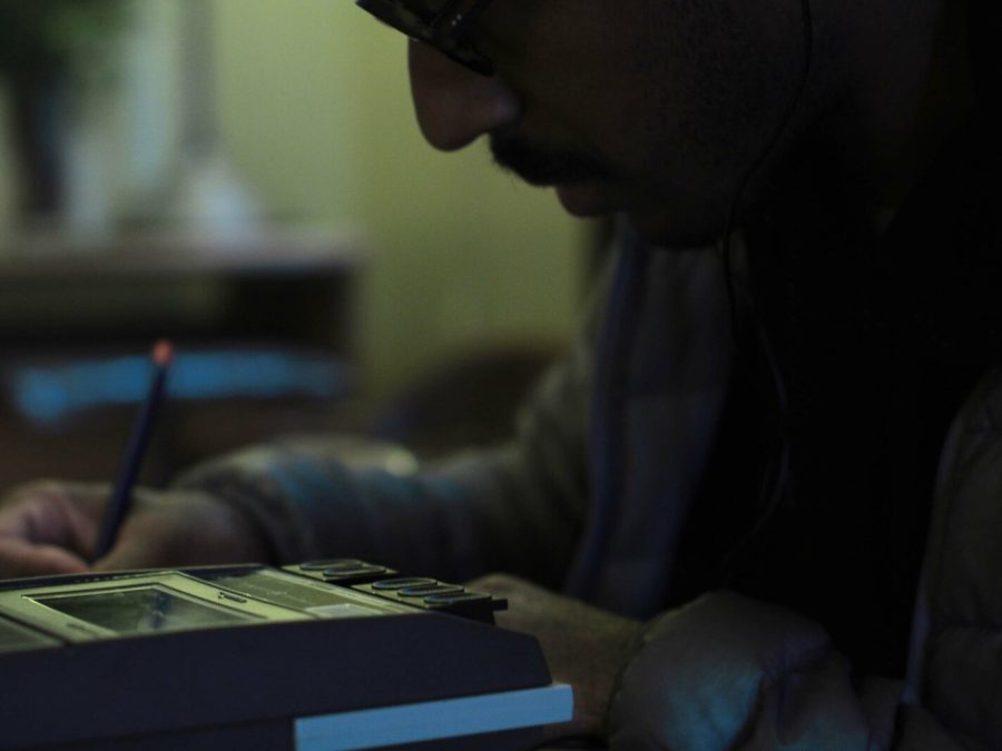 Close up of a man posed to write as he sits in front of a tape recorder.