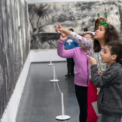 Children look and point at a black and white drawing of tropical trees and foliage that is displayed on two walls.