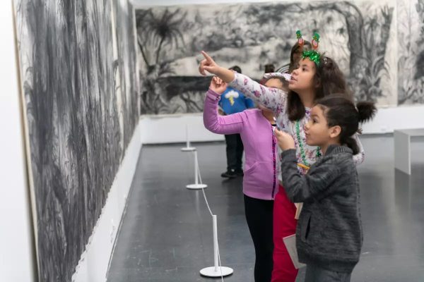 Children look and point at a black and white drawing of tropical trees and foliage that is displayed on two walls.