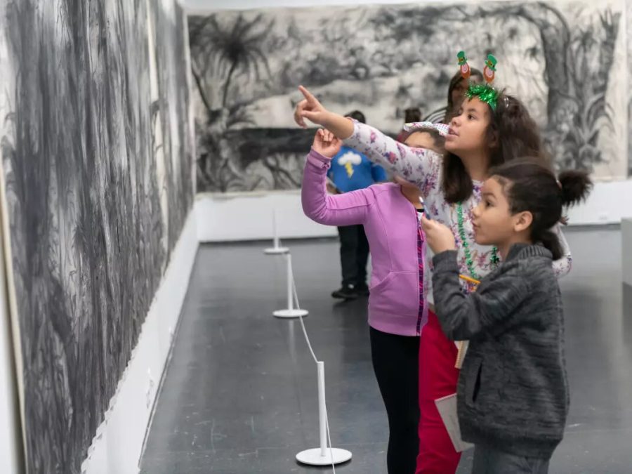 Children look and point at a black and white drawing of tropical trees and foliage that is displayed on two walls.