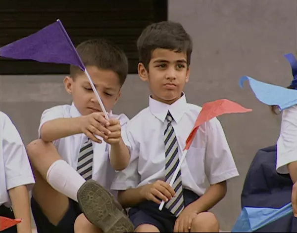 Two young boys wearing a uniform of white collared shirts and striped ties hold solid-colored pennants
