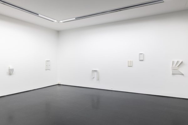 The corner of a gallery with several artworks hung on white walls