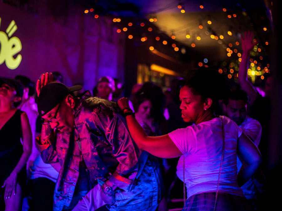 A group of people dance in a purple-lit room with red twinkle lights on the ceiling.