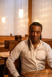 Photo of Willie Cole in a white long-sleeved collared shirt sitting in a bright restaurant.