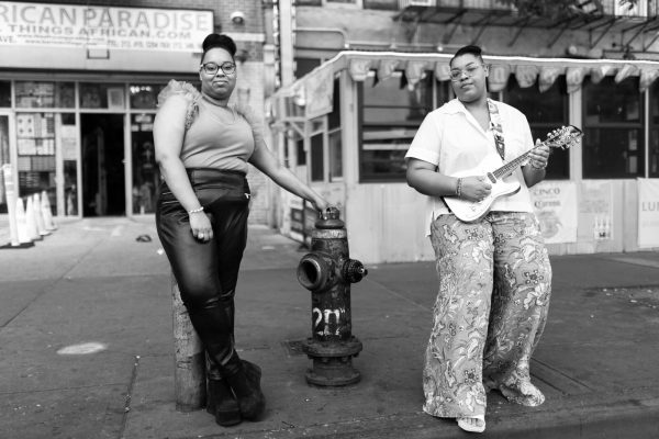 Black-and-white photo of two people posed next two a fire hydrant. One holds a guitar.