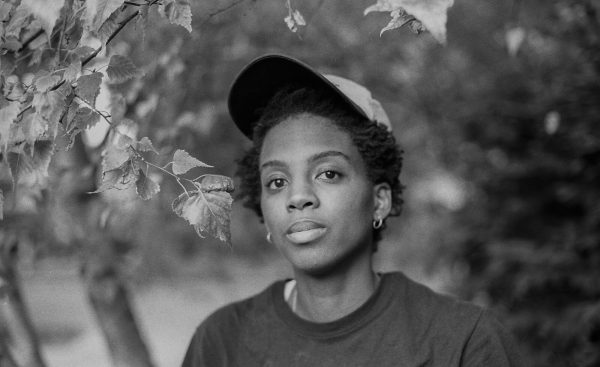 Black-and-white portrait of a Black woman with short hair among foliage.