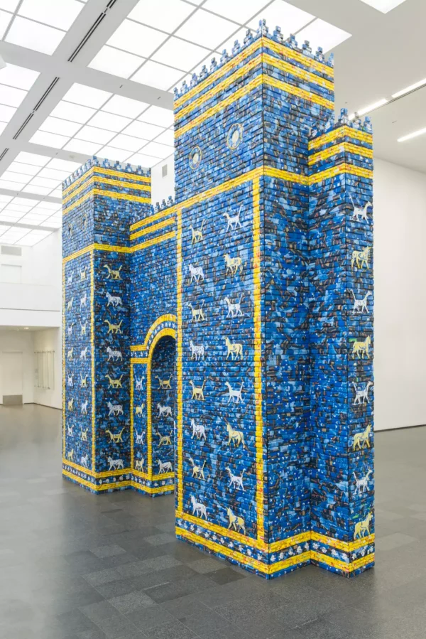 Installation view of a castle facade with crenelations, an arched doorway, and covered in blue and yellow paper–with stripes and columns of painted animals.