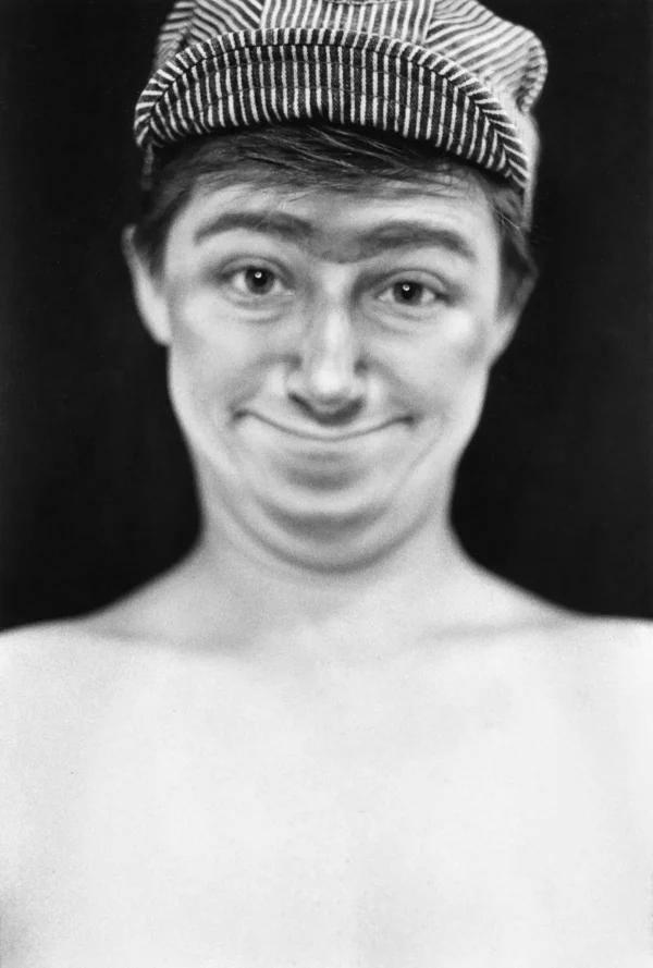 A portrait of a masculine-looking person with a goofy smile, double chin, sporting a striped hat in clear focus while the rest of the image recedes into a blur
