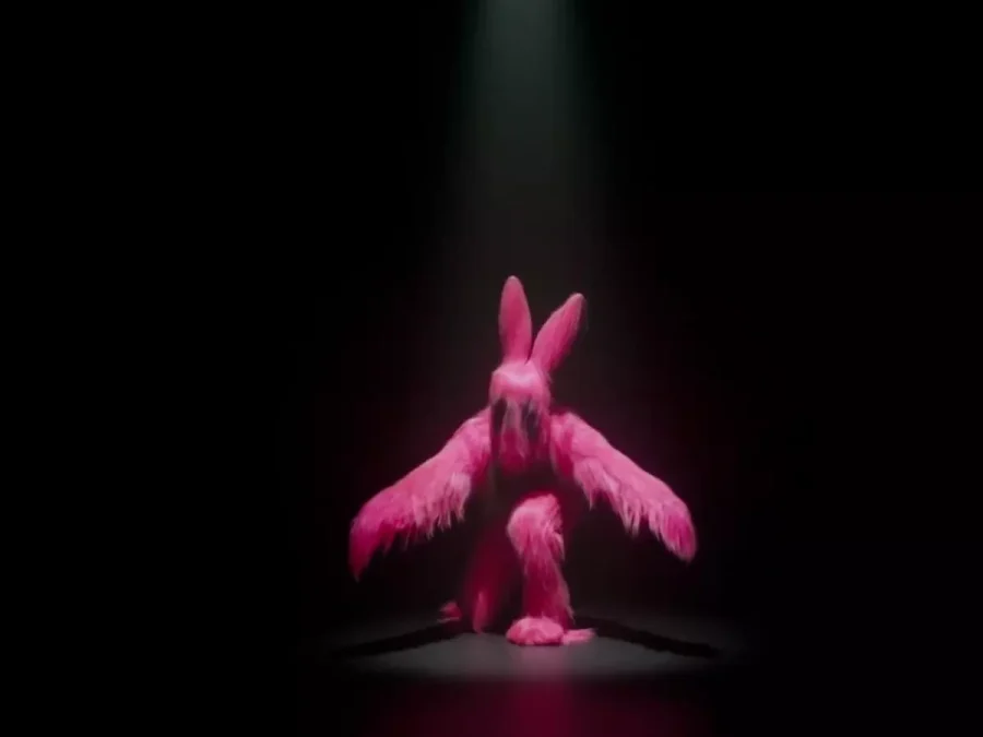 A performer costumed in a pink feathery bunny suit crouches with one leg forward, arms extended