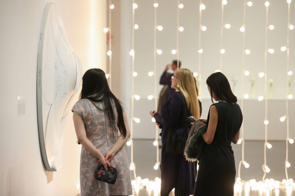 People looking at artwork in a gallery divided by strings of lights.