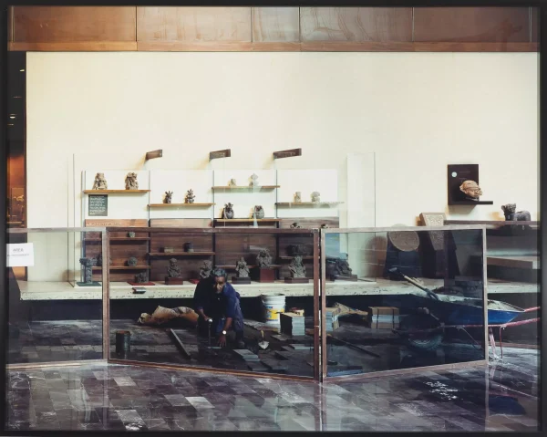 A man pauses his work of installing marble tiles to look at the camera while shielded by a glass barrier for visitors to watch