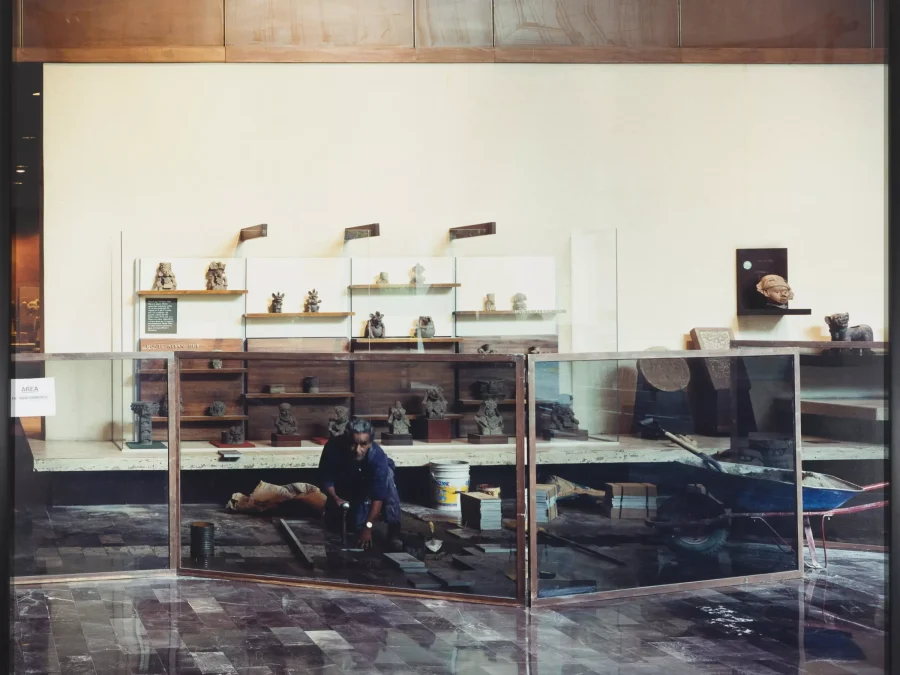 A man pauses his work of installing marble tiles to look at the camera while shielded by a glass barrier for visitors to watch