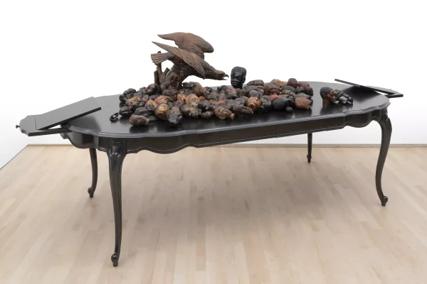 A carved eagle and 119 various carved heads on top of a table