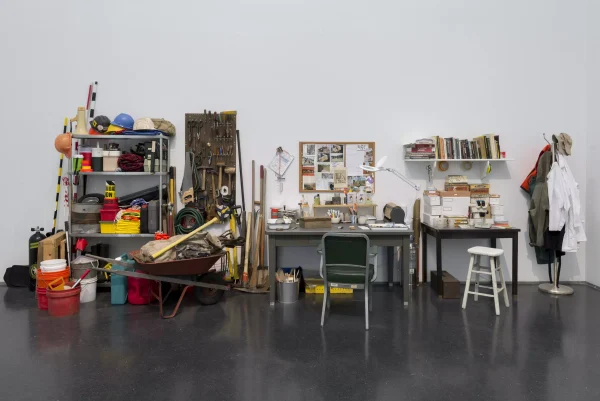 Desks and metal shelves full of tools, buckets, books and other equipment against a clean white wall