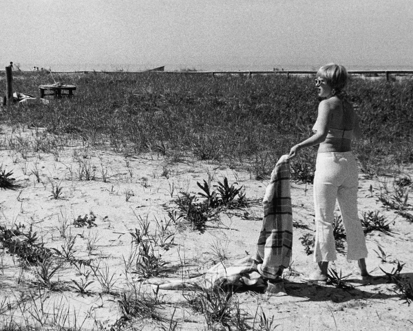 A woman standing on a sandy beach looks into the distance